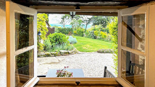 Blick durch ein Fenster auf einen Garten mit Rasenfläche, einem Kiesweg und einem Holzzaun.