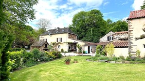 Ein traditionell gestaltetes Haus im europäischen Stil mit gepflegtem Rasen und Garten, umgeben von Bäumen und weiteren Gebäuden.