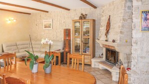 A cozy living room with a stone fireplace, a wooden cabinet with books, a sofa, and a dining table with chairs. - Gorgeous home in Saint Didier (Saint Didier)