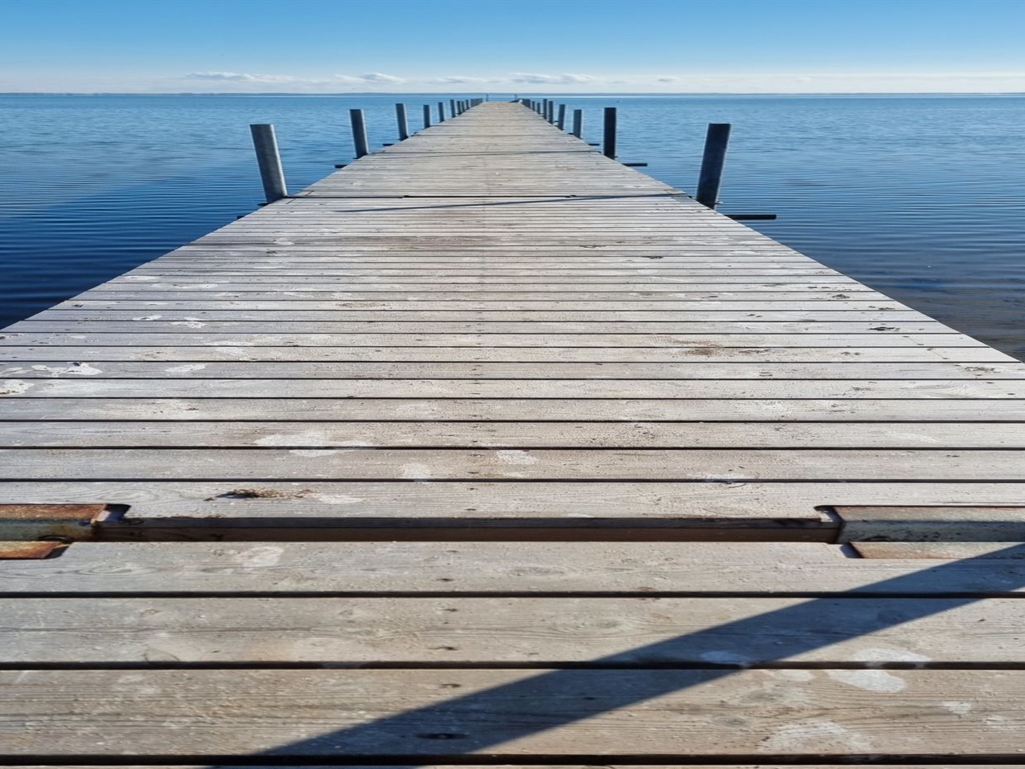Un muelle de madera se adentra en aguas tranquilas bajo un cielo despejado.