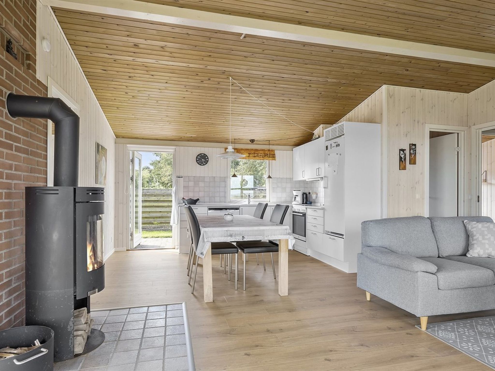 Een moderne keuken met een centraal eiland, een eethoek met een tafel en stoelen, een inbouwfornuis en een grijze bank in een woonkamer.