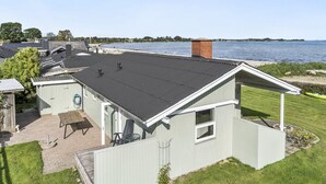 En fastighet vid kusten med en täckt uteplats, en liten byggnad med en skorsten och utsikt över havet.