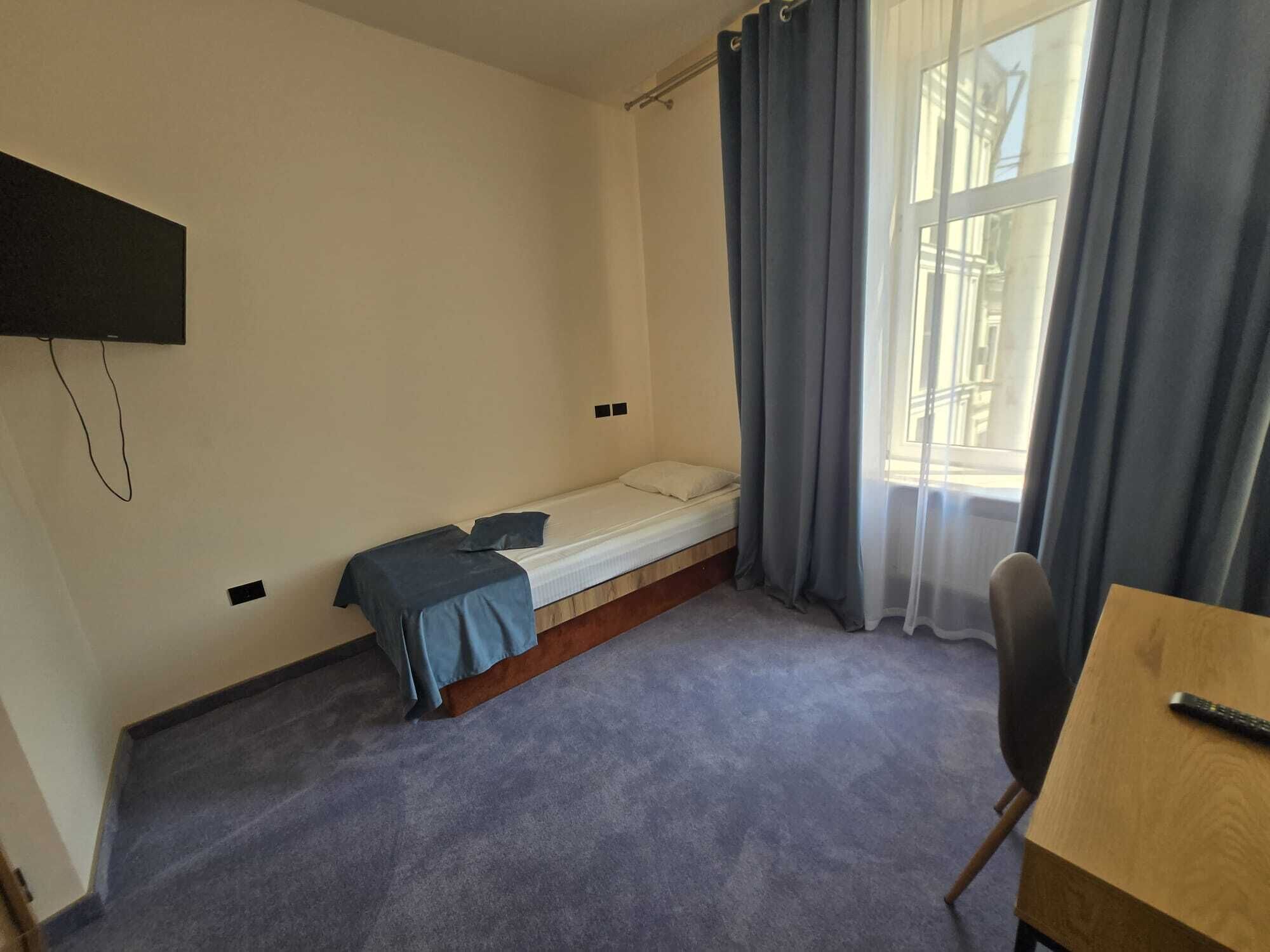 A small, sparsely furnished room with a single bed, a desk, and a chair.
