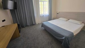 Een hotelkamer met een bed, een bureau, een aan de muur bevestigde televisie en een raam met gordijnen.