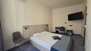 Een hotelkamer met een bed, een bureau, een stoel, een aan de muur bevestigde televisie en een airconditioner.