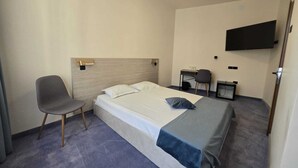 Een hotelkamer met een bed, een stoel, een bureau en een televisie aan de muur.