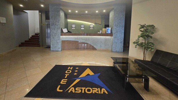 Een hotel lobby met een receptiebalie, een trap en een receptiegedeelte met een klok en een plant.