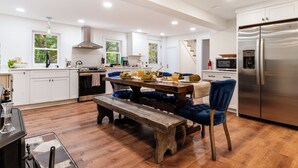 Une cuisine moderne avec des meubles blancs, un réfrigérateur en acier inoxydable et une table à manger en bois, assortie de chaises bleues.