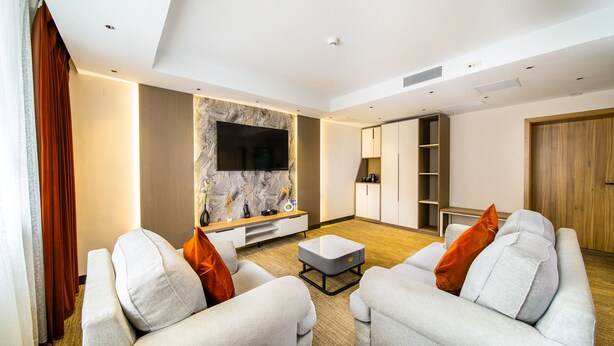 Ein modernes Wohnzimmer mit einem Flachbildfernseher, zwei Sofas mit orangefarbenen Kissen, einem Couchtisch und eingebauten Regalen.