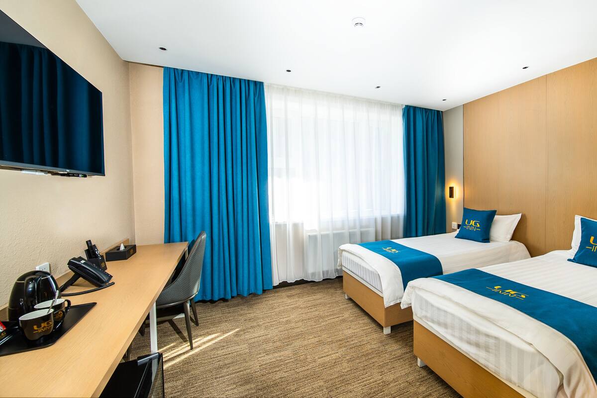 Hotellihuone, jossa on kaksi sänkyä, työpöytä, tuoli, televisio ja ikkuna, jossa on verhot.