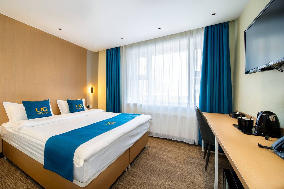 Hotellihuone, jossa on sänky, työpöytä, televisio ja kahvinkeitin.