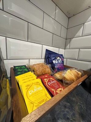 A tray with various packaged food items, including snacks and bread, in a kitchen setting with white tiled walls. - Stylish studio with wet room & kitchen (London)