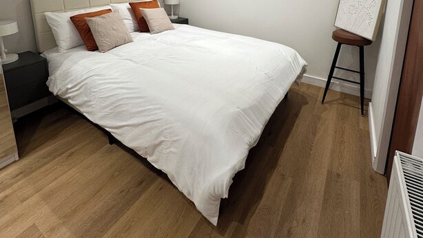 Een slaapkamer met een bed, nachtkastjes, een schilderij en een radiator.