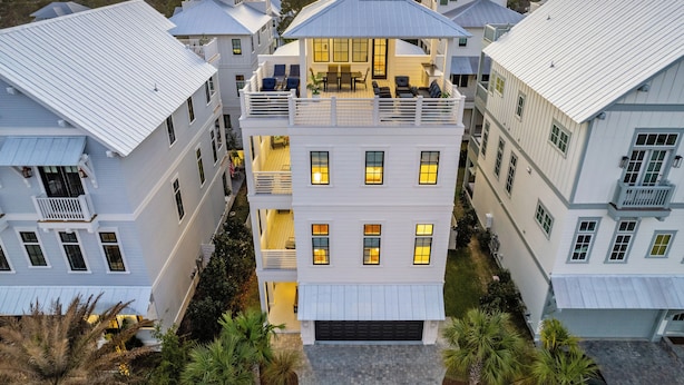 A multi-story residential building with a prominent balcony on the second floor, surrounded by similar structures. - Beach Sea-ker's Retreat by AvantStay | Rooftop Deck w/ Views, Pool, Luxury 5BDR (Inlet Beach)