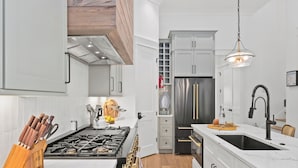 A modern kitchen with white cabinetry, a stainless steel refrigerator, a gas stove, and a black sink. - Beach Sea-ker's Retreat by AvantStay | Rooftop Deck w/ Views, Pool, Luxury 5BDR (Inlet Beach)