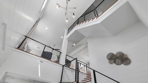 A multi-level interior with white walls, a staircase with black railings, and a modern chandelier. - Beach Sea-ker's Retreat by AvantStay | Rooftop Deck w/ Views, Pool, Luxury 5BDR (Inlet Beach)