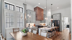 A modern kitchen with a central island, wooden cabinets, and a stainless steel refrigerator. - Beach Sea-ker's Retreat by AvantStay | Rooftop Deck w/ Views, Pool, Luxury 5BDR (Inlet Beach)