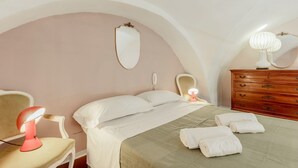 Een slaapkamer met een bed, nachtkastje, lamp, kaptafel en een spiegel aan de muur.