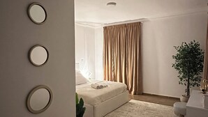 Un dormitorio moderno con una cama, una mesita de noche, una planta en maceta y un amplio ventanal con cortinas.
