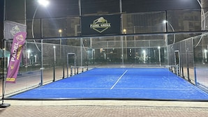 Una cancha deportiva cubierta con superficie azul, rodeada por una red y un cartel que dice 'PADEL ARENA'.