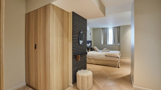 A modern bedroom with a wooden wardrobe, a small stool, a bed with a white duvet, and a window with curtains. - Wonderful flat Luxembourg Park St Germain des près (Paris)