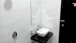 A bathroom with a white marble wall, a black countertop, a white sink, a mirror, and a door. - Gaura Resort (Mohanlalganj)