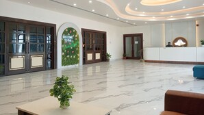 A hotel lobby with a reception desk, a green floral wall, and a marble floor. - Gaura Resort (Mohanlalganj)