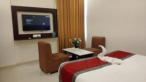A hotel room with a bed, a TV mounted on the wall, a small table with a vase of flowers, and two armchairs. - Gaura Resort (Mohanlalganj)