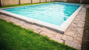 A rectangular swimming pool with a stone border, surrounded by a grassy area and a low concrete wall. - Tulia Homestays (Nakuru)