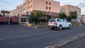 A multi-story residential building with a gated entrance, a bench, and a white SUV parked on the street. - Tulia Homestays (Nakuru)