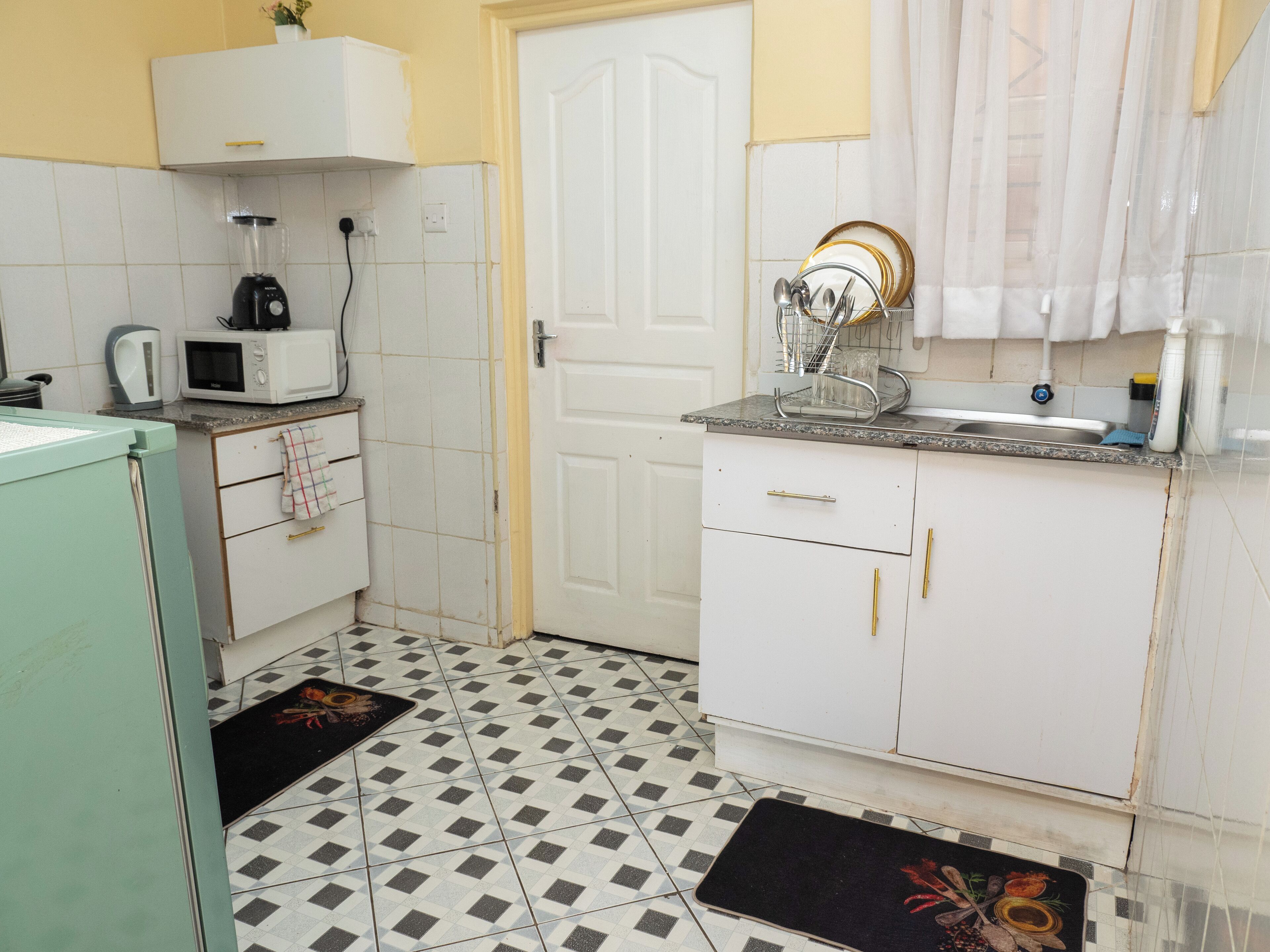 A compact kitchen with white cabinets, a microwave, a kettle, and a sink.