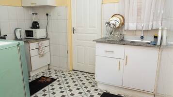 A compact kitchen with white cabinets, a microwave, a kettle, and a sink.