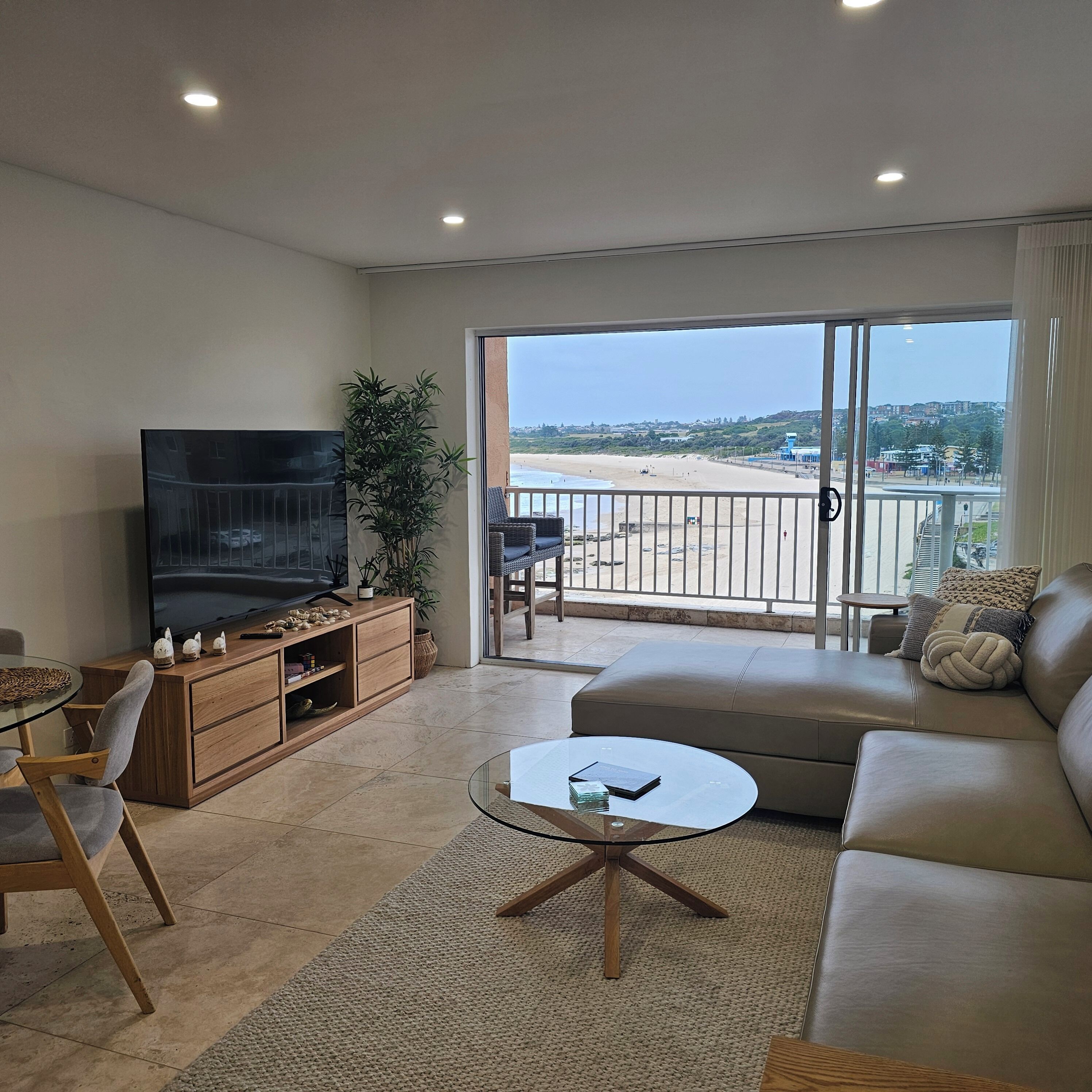 Sala de estar con televisor, sofá y vista al mar.