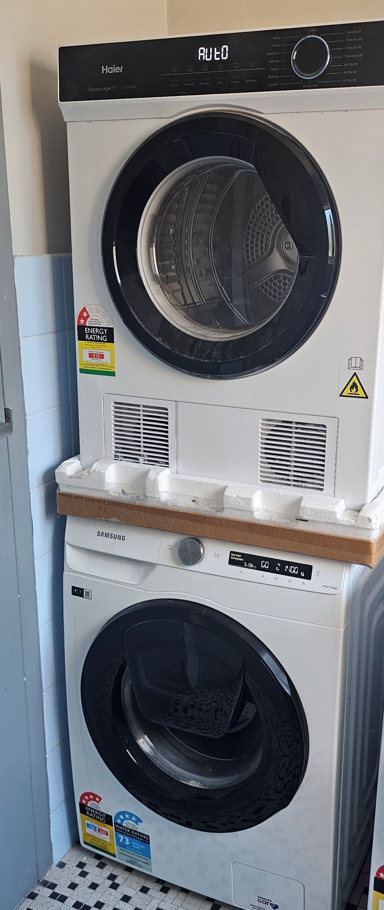 Two stacked front-loading washing machines, one Haier and one Samsung, with energy and water efficiency ratings.