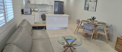 A modern living room with a sofa, a glass coffee table, and a dining area with a round table and chairs.
