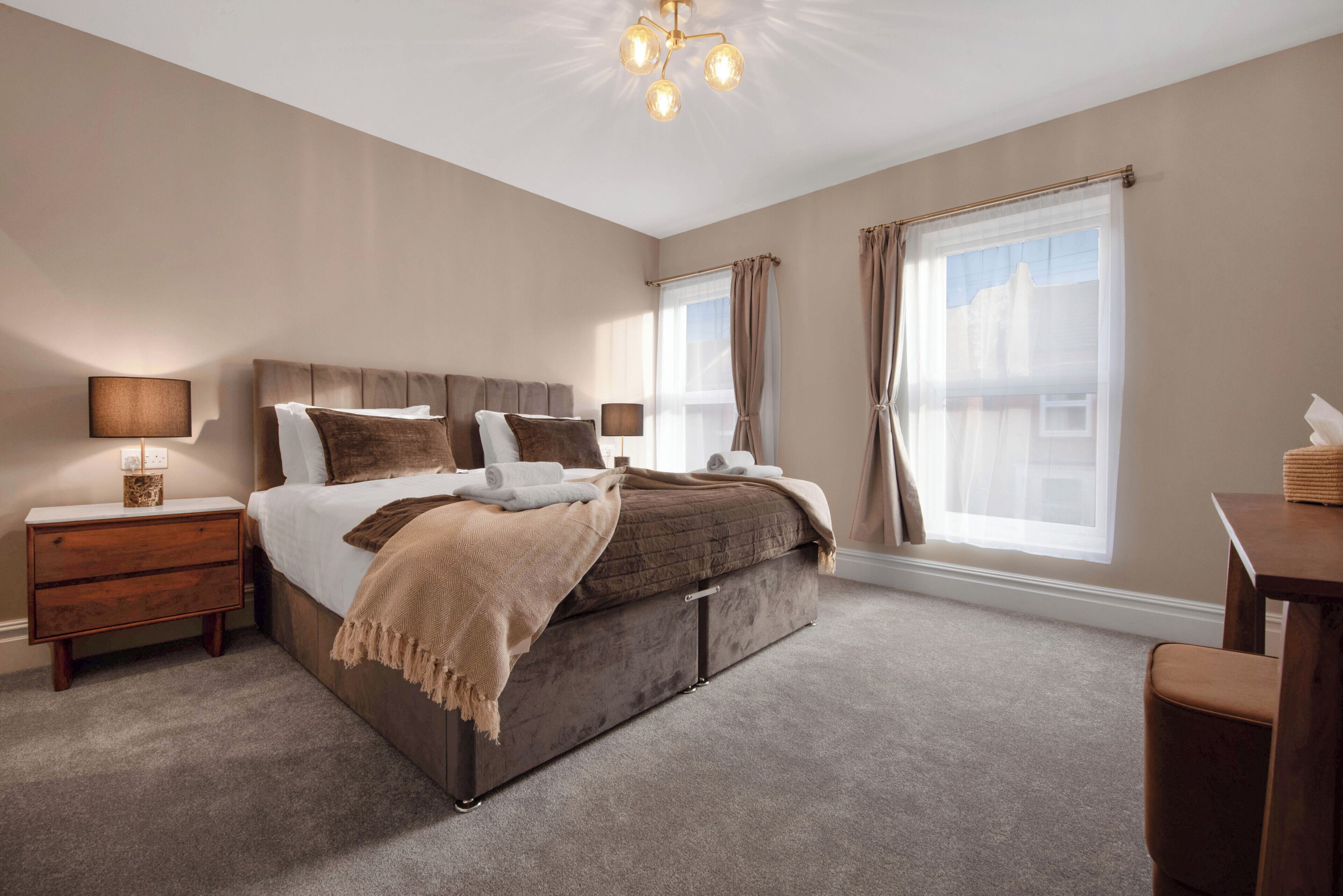 A bedroom with a large bed, bedside tables, a desk, and a window with curtains.