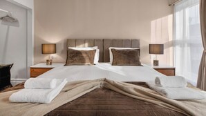 Quarto de hotel com cama grande, duas mesas de cabeceira com luminárias, um cabideiro e uma janela com cortinas.