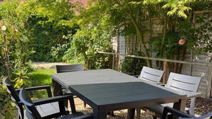 Um pátio externo com mesa e cadeiras, cercado por vegetação e uma parede de pedra.