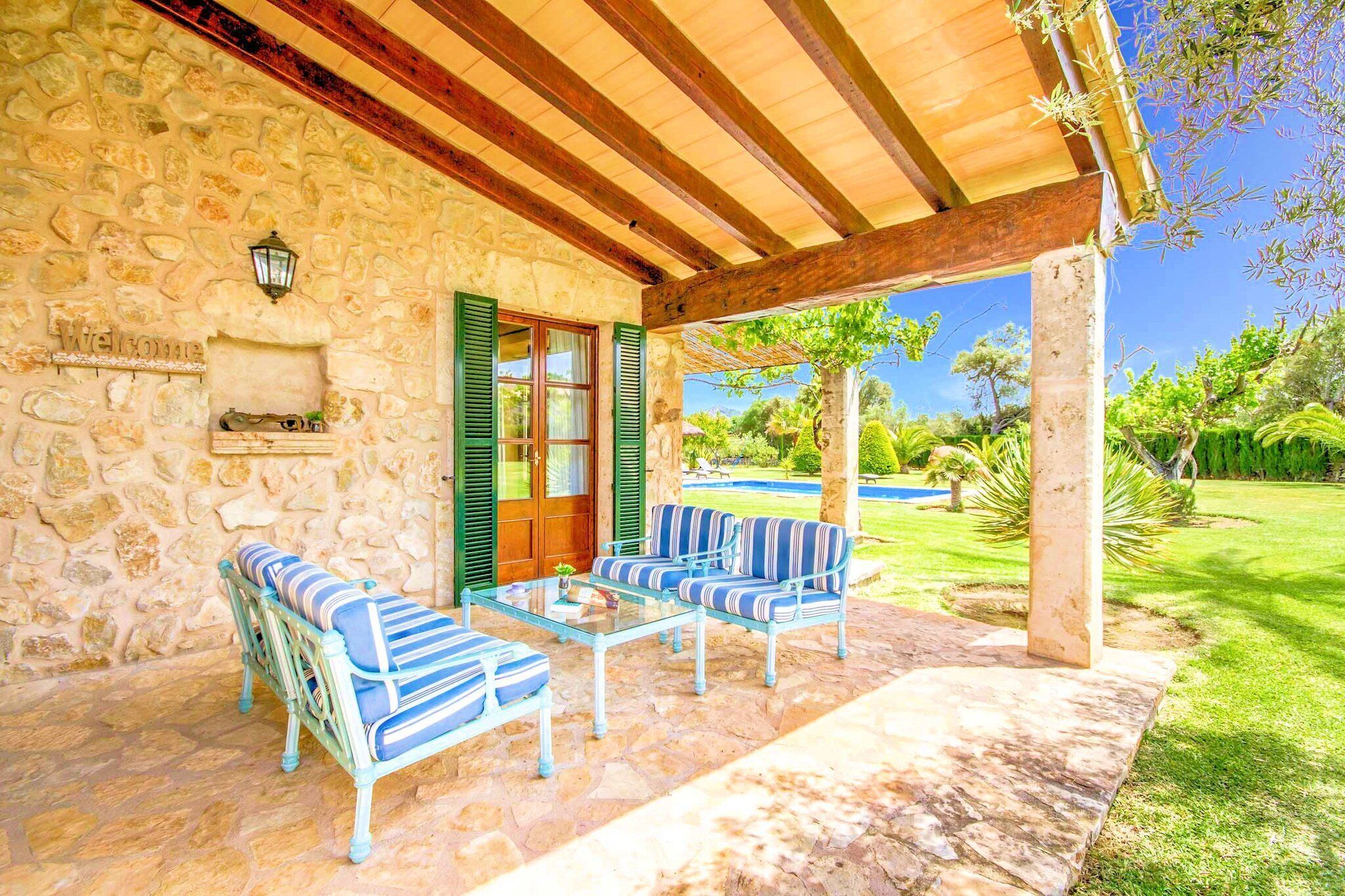 A stone building with a wooden pergola, outdoor seating, and a view of a garden.