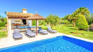 A pool area with lounge chairs and a thatched umbrella, surrounded by a well-maintained lawn and palm trees. - Finca Roig Petit | Mallorcan Charm in Pollensa | Private Pool & Tranquil. (Pollensa)