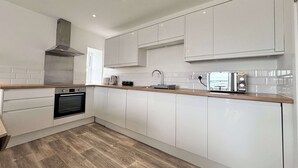 Een moderne keuken met witte kasten, een ingebouwde oven, een roestvrijstalen afzuigkap en een magnetron op het aanrecht.
