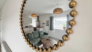 Een woonkamer met een grote spiegel, een bank, een bijzettafeltje en een hanglamp.