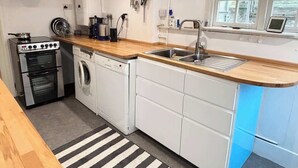 A compact kitchen with a stove, oven, washing machine, and a sink. - Unique Artsy Home on the Penzance Promenade (Penzance)