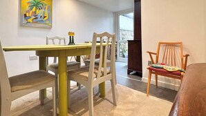 A dining area with a high table and chairs, a painting on the wall, and a view through a glass door. - Unique Artsy Home on the Penzance Promenade (Penzance)
