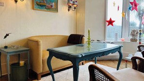 A cozy living room with a sofa, a glass-top table, and wall-mounted lighting. - Unique Artsy Home on the Penzance Promenade (Penzance)