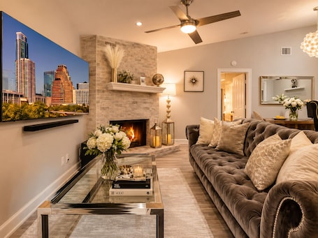 A modern living room with a fireplace, a sofa, a coffee table, and a cityscape painting.. Domain District Gem • Stylish 2BR/2BA • Perfect Location