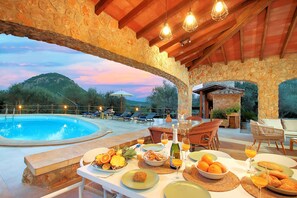 Un área de comedor al aire libre con un arco de piedra, una piscina y sillones de descanso.