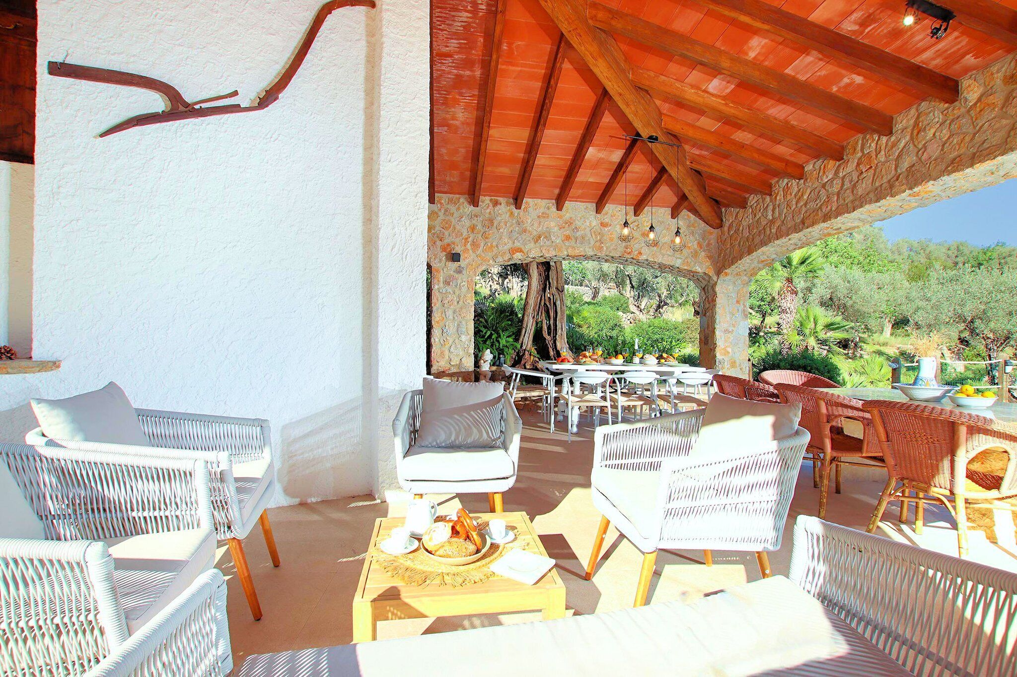 Une terrasse extérieure aménagée avec des meubles en osier, des arches en pierre et une vue sur la verdure.