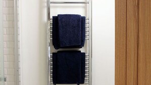 Une salle de bain avec un porte-serviettes en métal sur lequel sont posées deux serviettes bleu foncé, des carreaux de sol à motifs et une porte en bois.