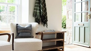 Una habitación acogedora con un sillón blanco, un banco de madera y una manta verde a cuadros.